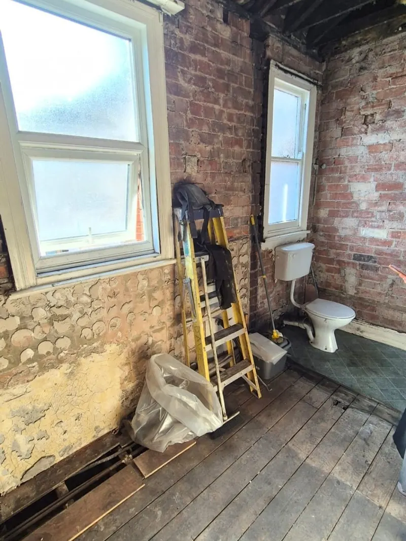 A bathroom stripped to bare brick with the floorboards lifted and the original toilet still in place