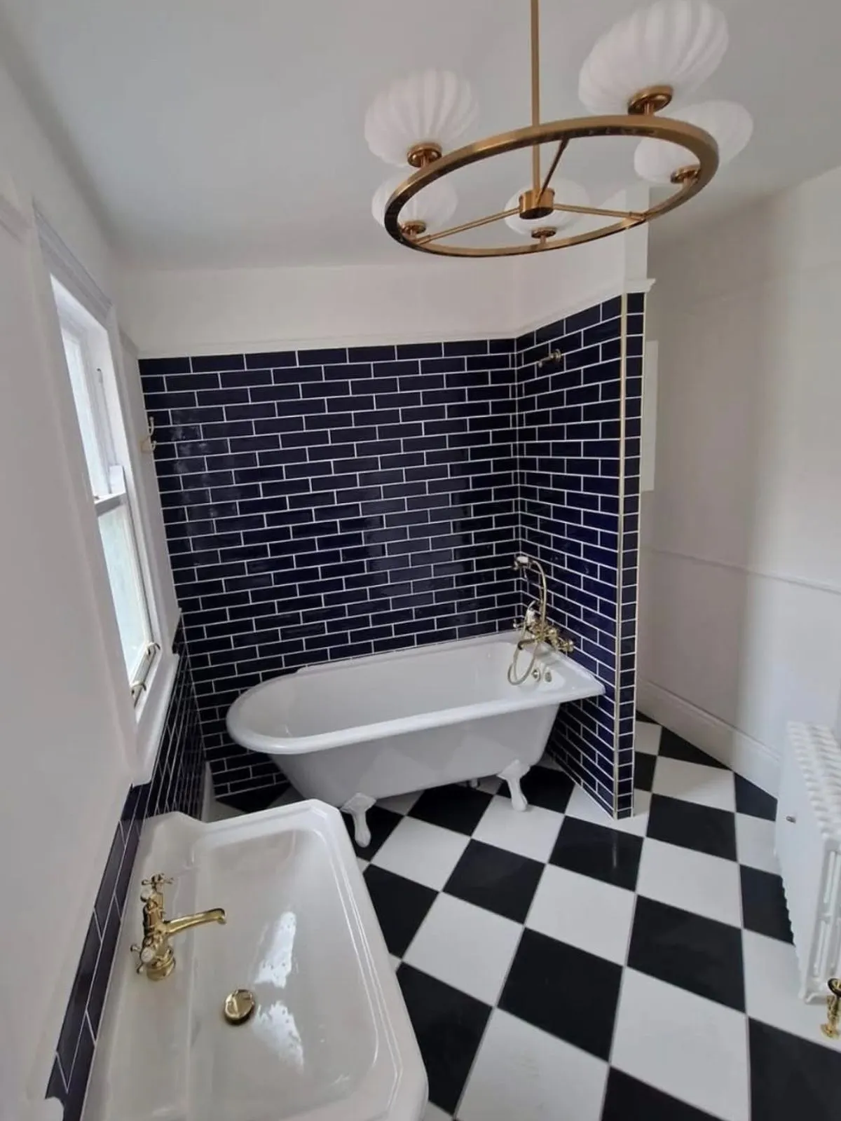 A roll top bath on claw feet against navy metro tiling with a black and white checkerboard floor