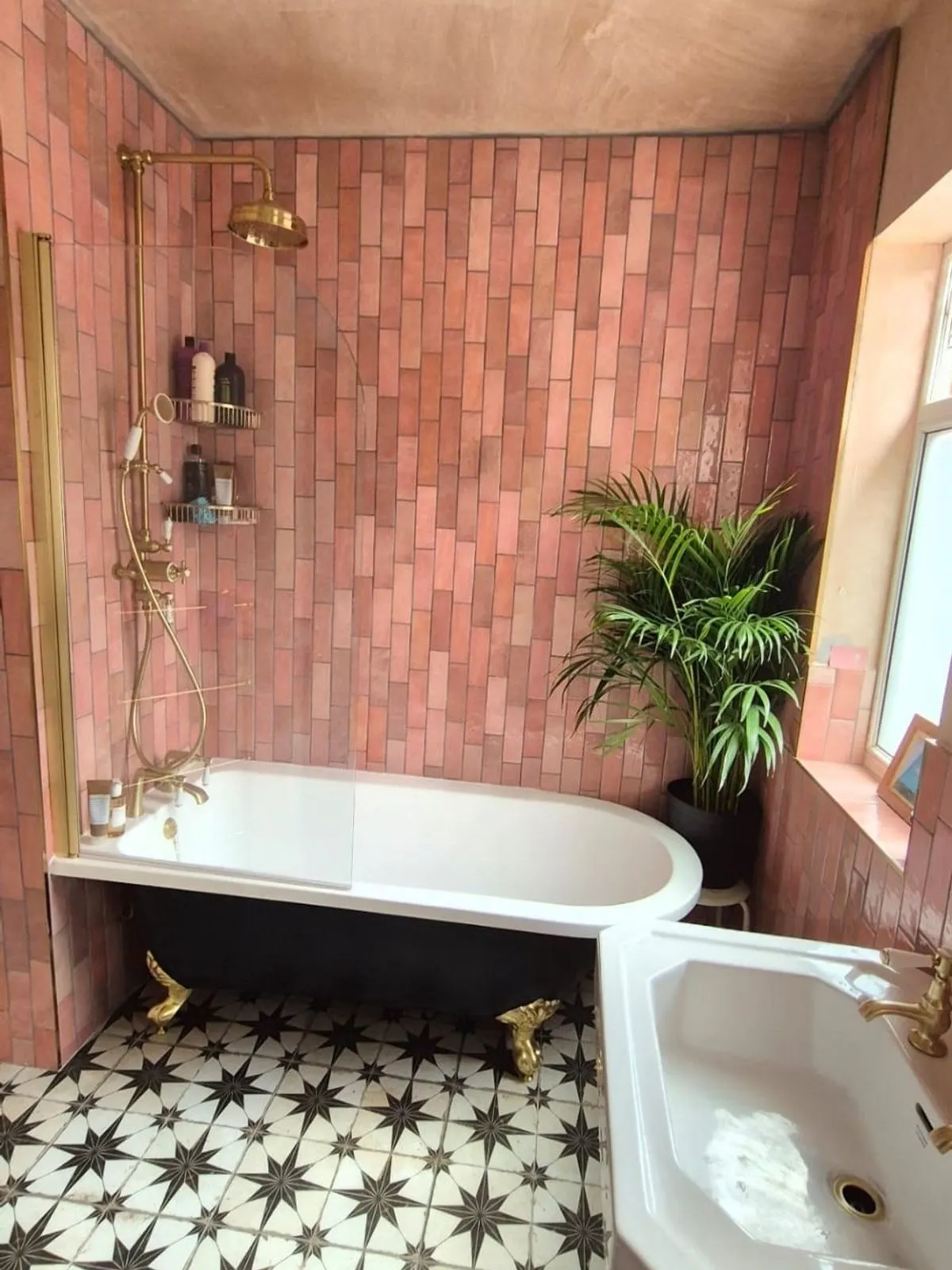 A black roll top bath with brass feet against pink zellige tiling, with a star patterned tile floor
