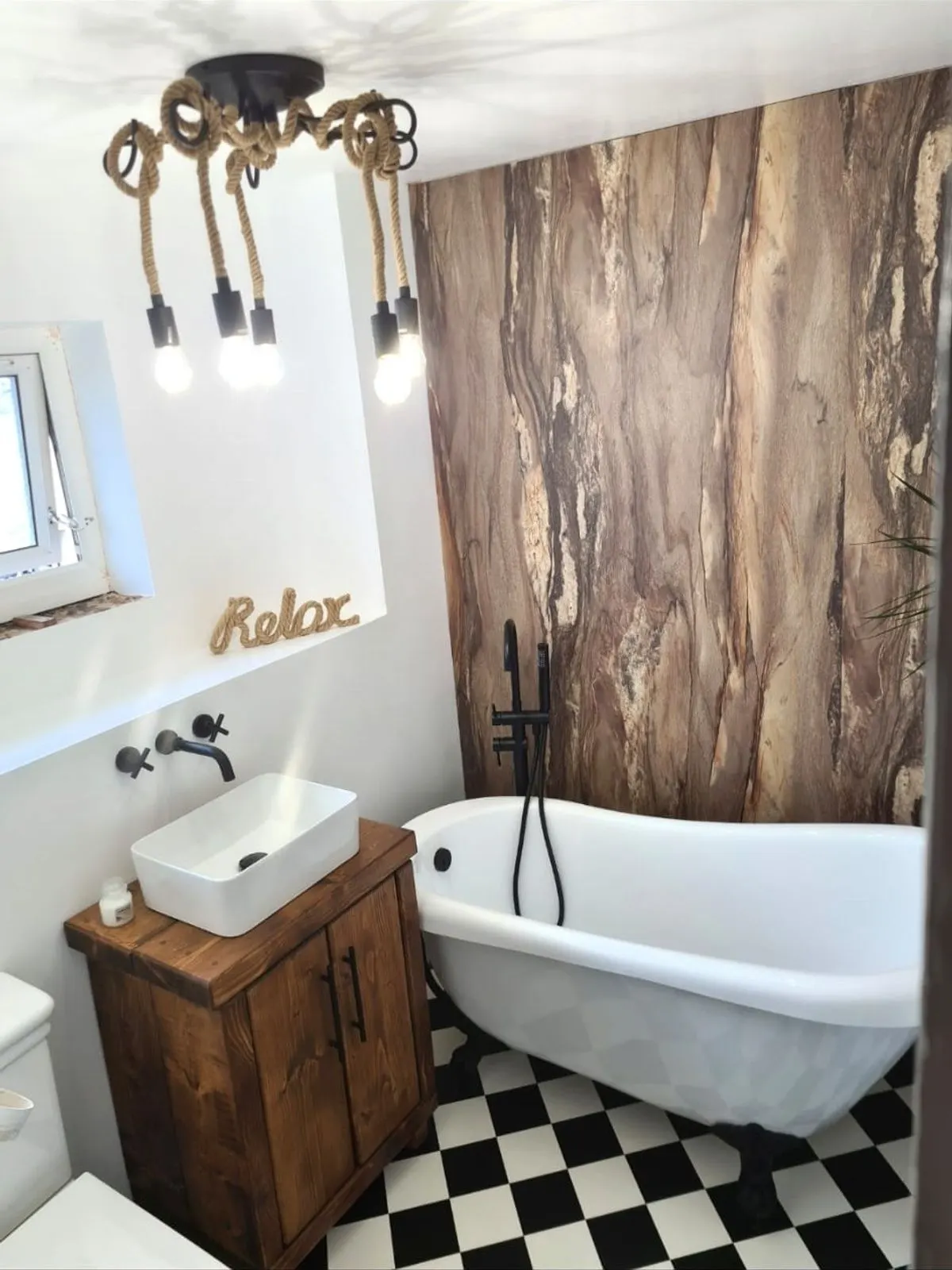 A roll top bath beside a reclaimed timber vanity, with rope pendant lights and a stone effect feature panel