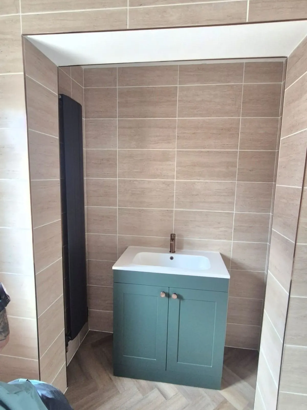 A green vanity unit with copper tap and a black vertical radiator on herringbone flooring