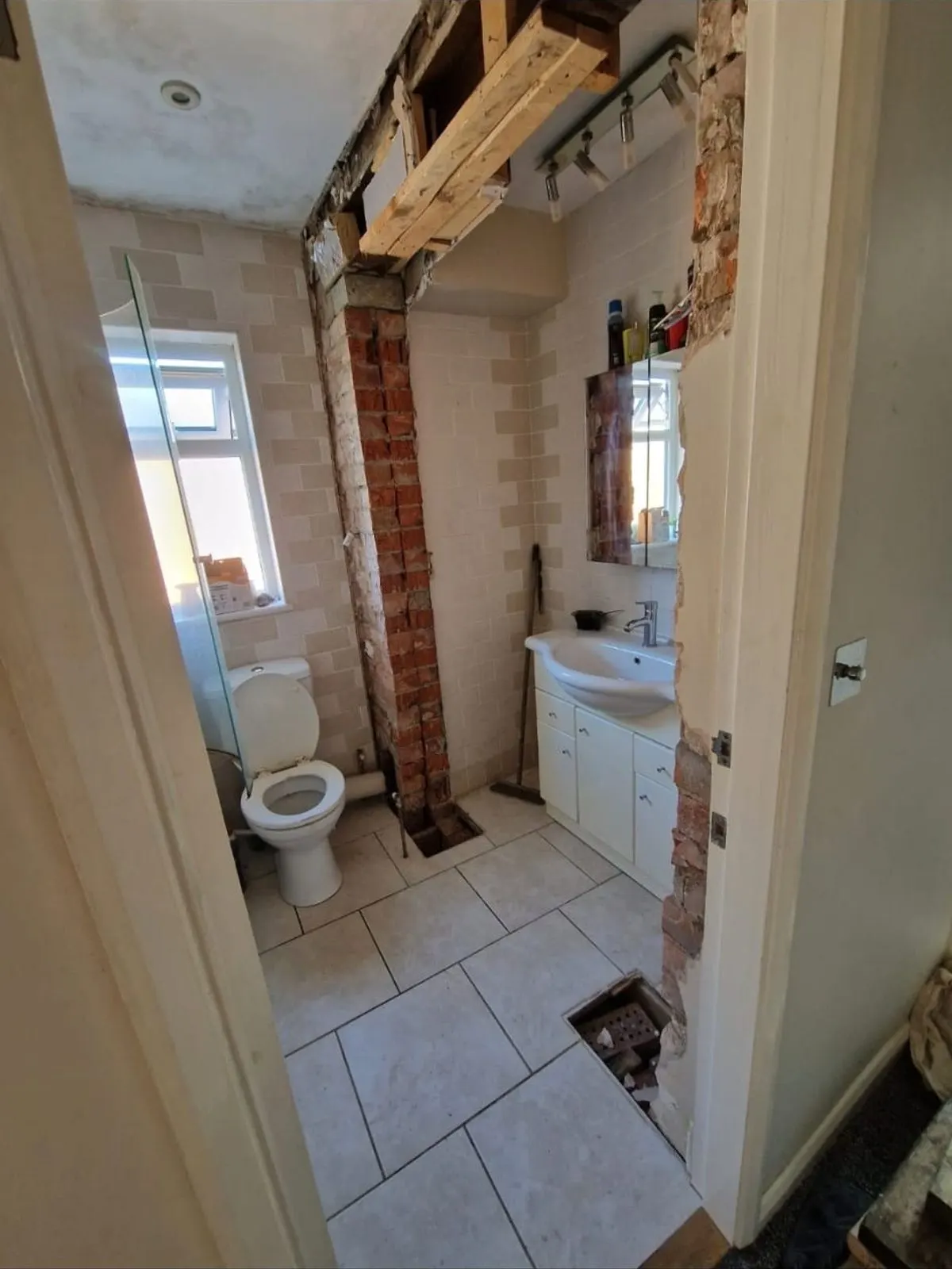 A bathroom part way through strip-out with tiling removed and brickwork exposed around the doorway
